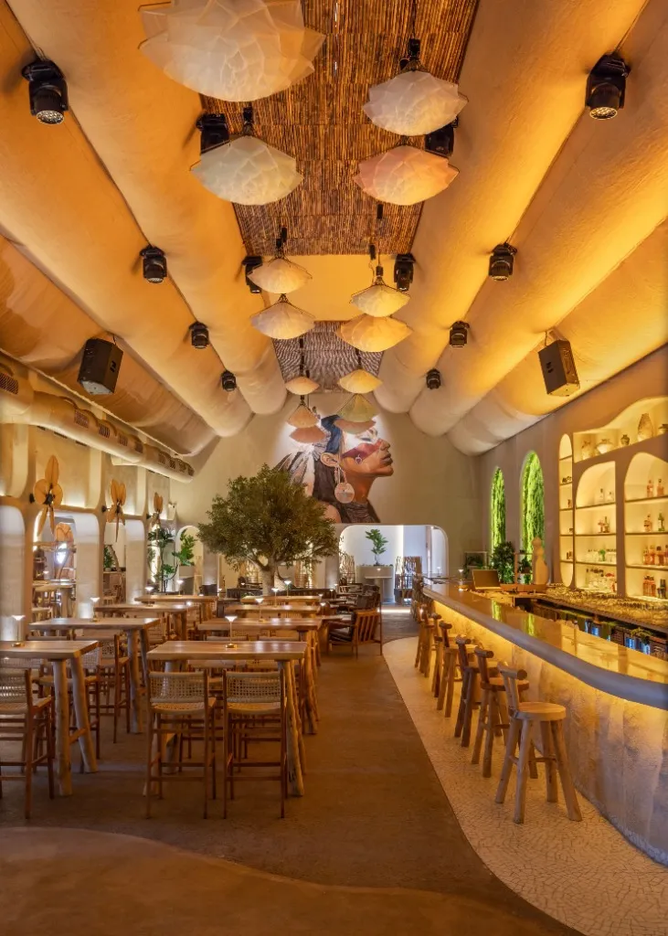 Long restaurant hall with vaulted plaster ceilings, lotus shaped pendant lights, a curved bar and a large painted mural