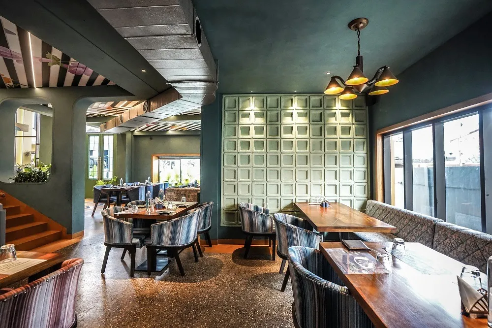 Restaurant dining room with teal walls, a sculpted white panel wall, timber tables and striped upholstered chairs