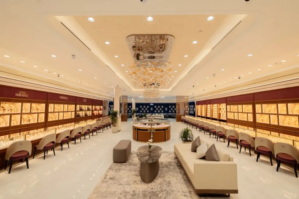 Jewellery showroom with gold lit display cabinets along both walls, cream lounge seating and a crystal chandelier in a coffered ceiling
